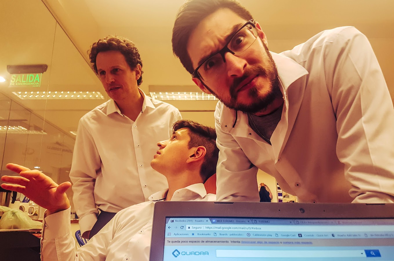 Tres personas alrededor de una notebook en la oficina, de noche